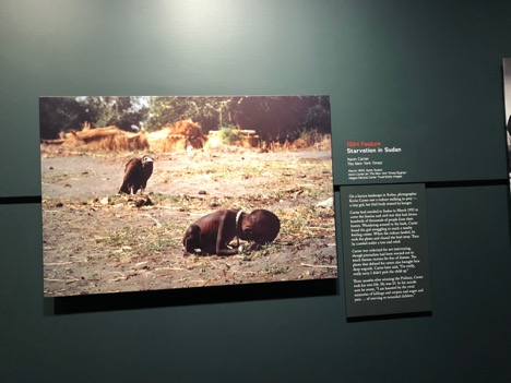 Picture of a Pulitzer Prize featured photo, Starvation in Sudan (1994). A small, frail child sits with her head down as a vulture preys on her from behind. 