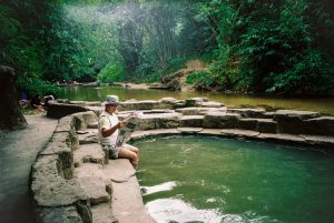 Person sitting along the edge of the Annah Rais hotspring pool reading the news in Sarawak, Malaysia.